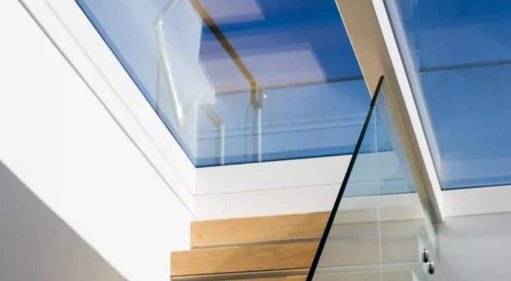 close up photo of wooden stairs leading to a sliding rooflight, blue sky can be seen through the glass