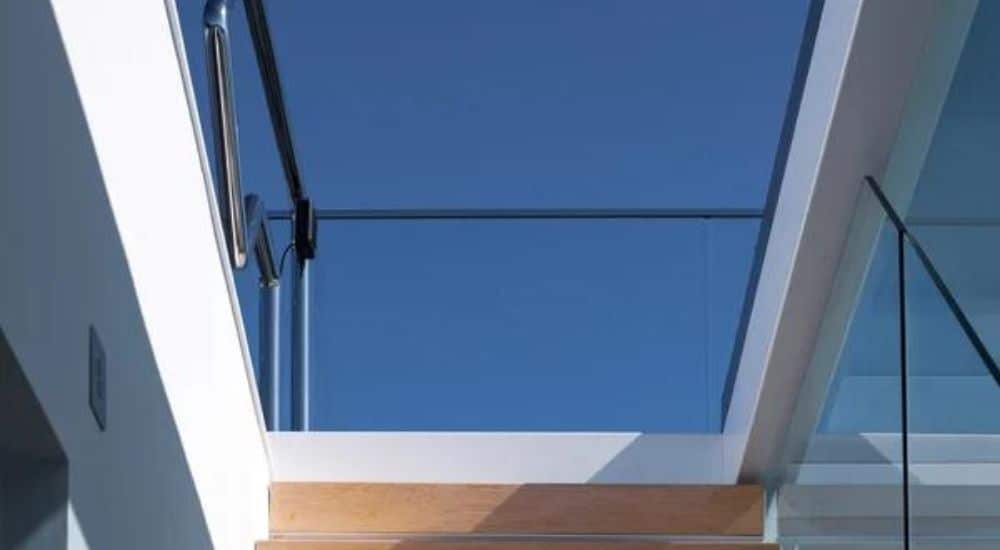 close up photo of stairs leading to a roof terrace through a sliding rooflight, blue clear skies can be seen through the glass