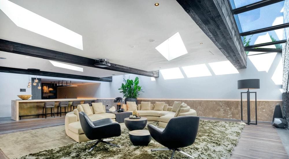 multipart rooflight installed above a modern reception area, sofas and chairs surround a deep coffee table and a bar to the left
