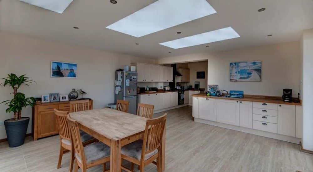 three fixed rooflights installed above a kitchen and dining area, white cabinets and wooden countertops surround the wooden table and chairs