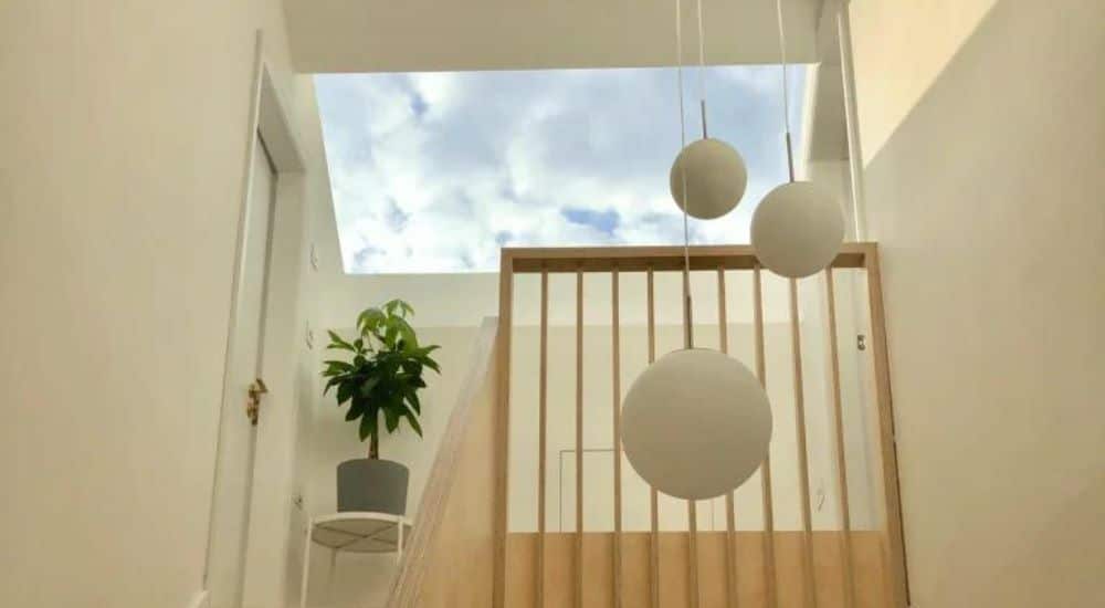 roof window installed in pitched roof, lights hang down by the cream walls and a potted plant on a white stall sits under the big roof window