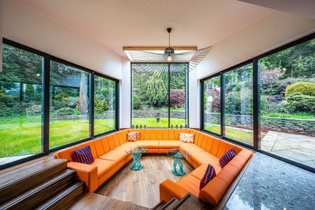 living room with a long, curving orange sofa surrounded by windows with views to the green garden