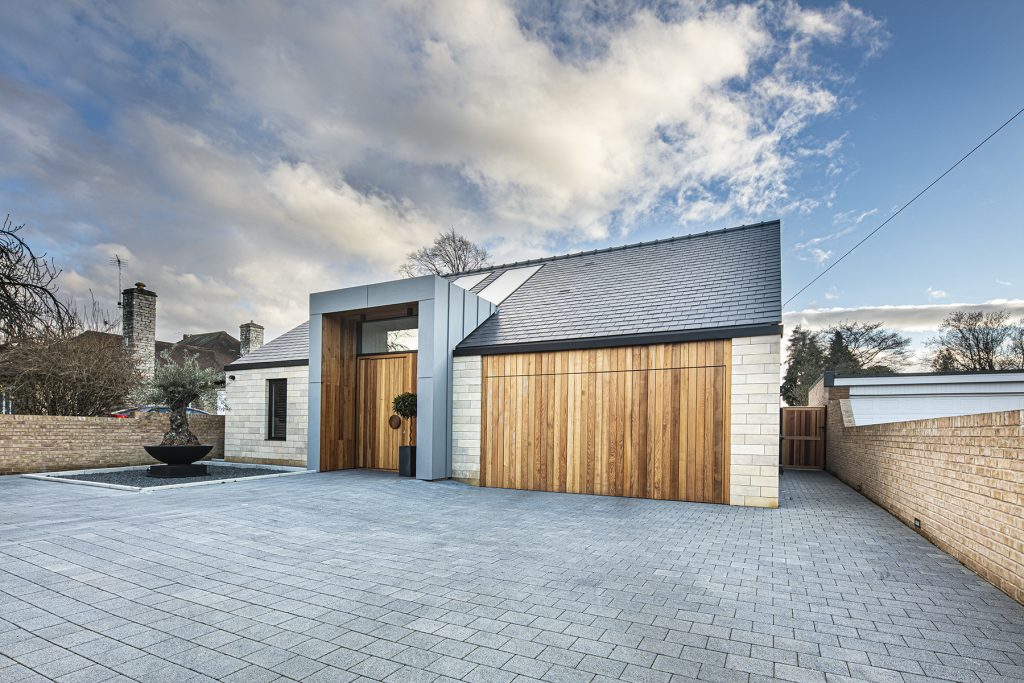 exterior of modern building with a driveway of grey tiles and a wooden fence and door