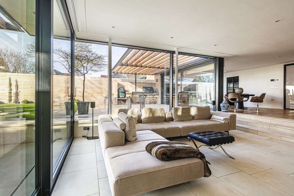 modern living room with a cream sofa and steps lead up to wooden floor and a small dining table, panoramic windows provide views of the outside garden