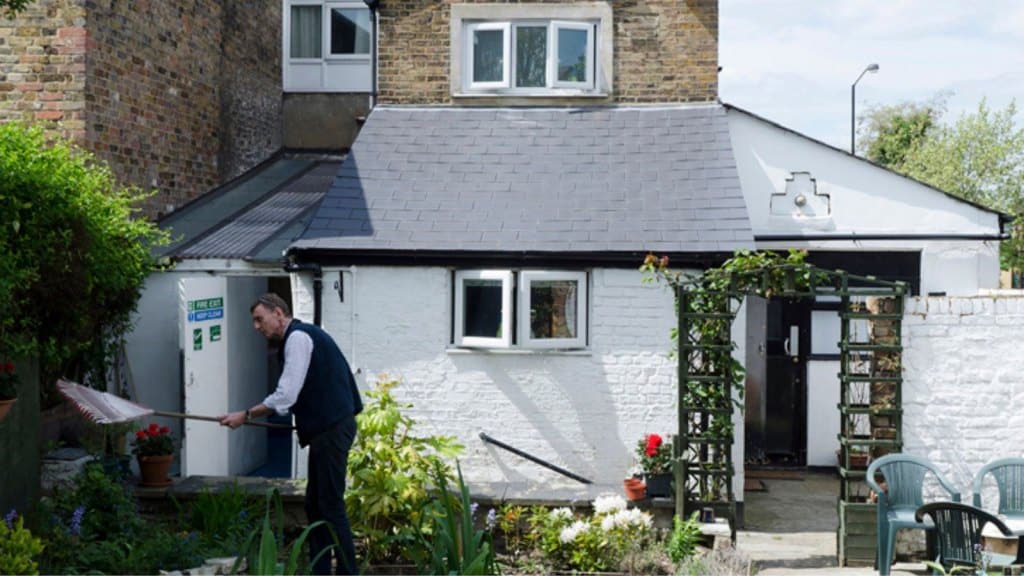 Man working on the garden of a small charity building with a white extension