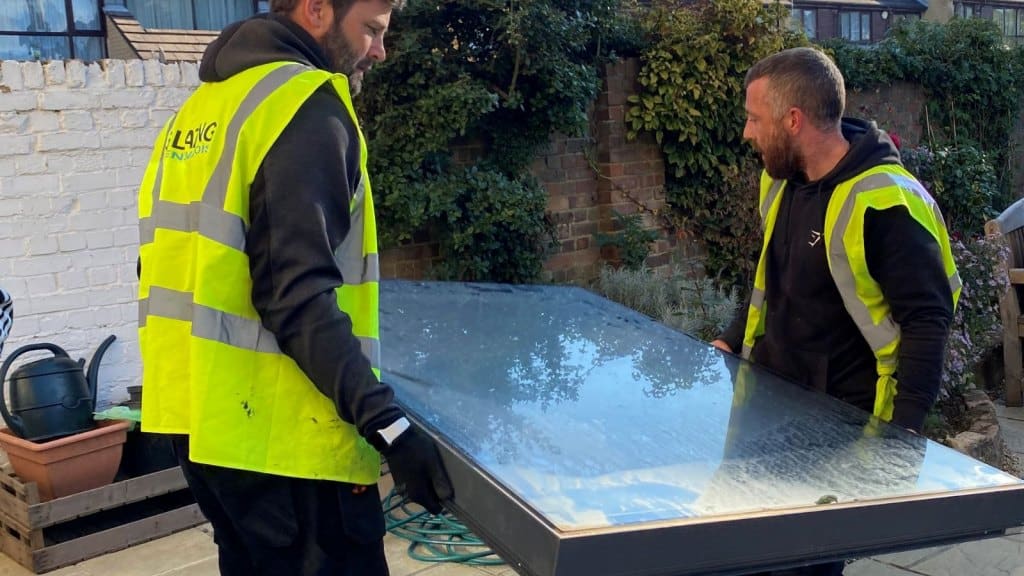 two men in Glazing Renovations branded hi-viz jackets lifting a roofligh ready for installation