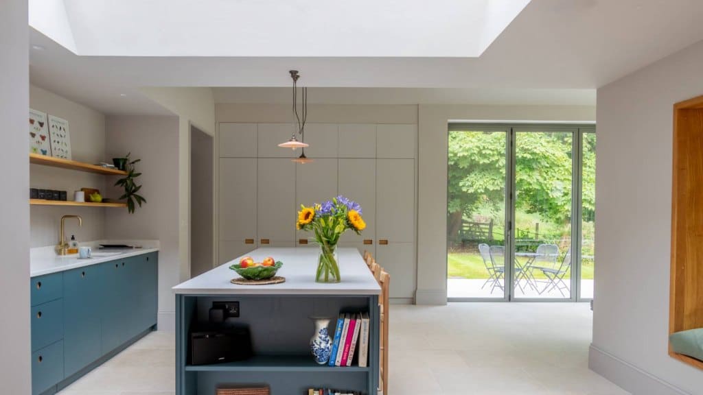 Rooflight installed above a kitchen island adorned by a vase of flowers, blue cabinets and accents