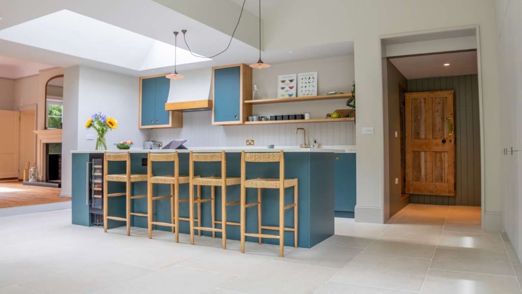 Modern kitchen with blue accents and wooden chairs at the breakfast bar, rooflight installed in the kitchen brings in daylight