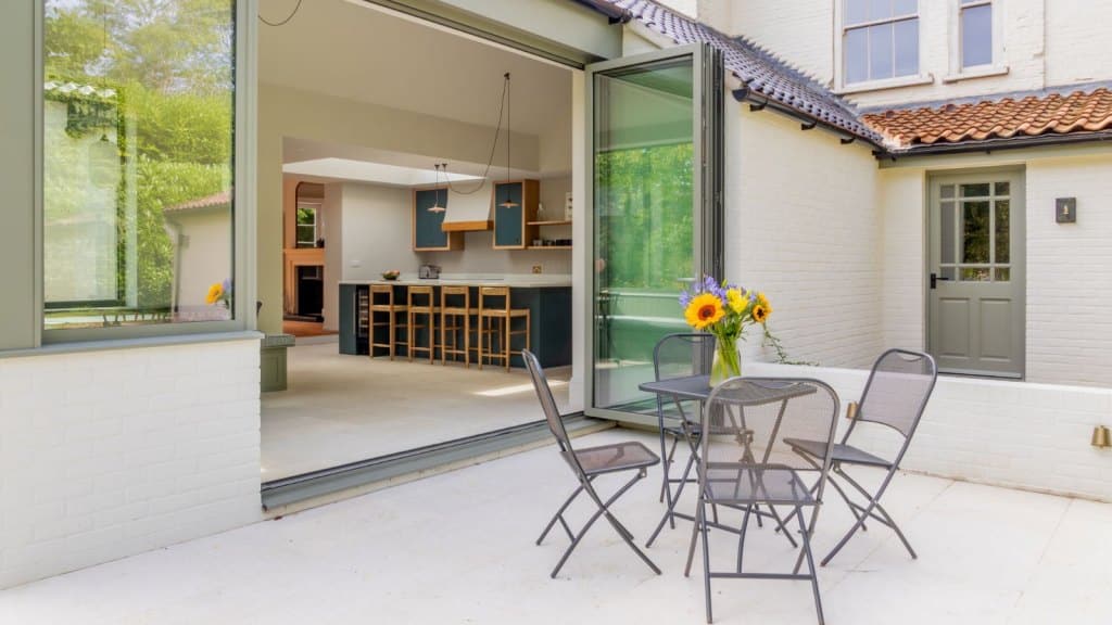 Modern extension with garden patio, grey metal patio furniture features a vase of flowers