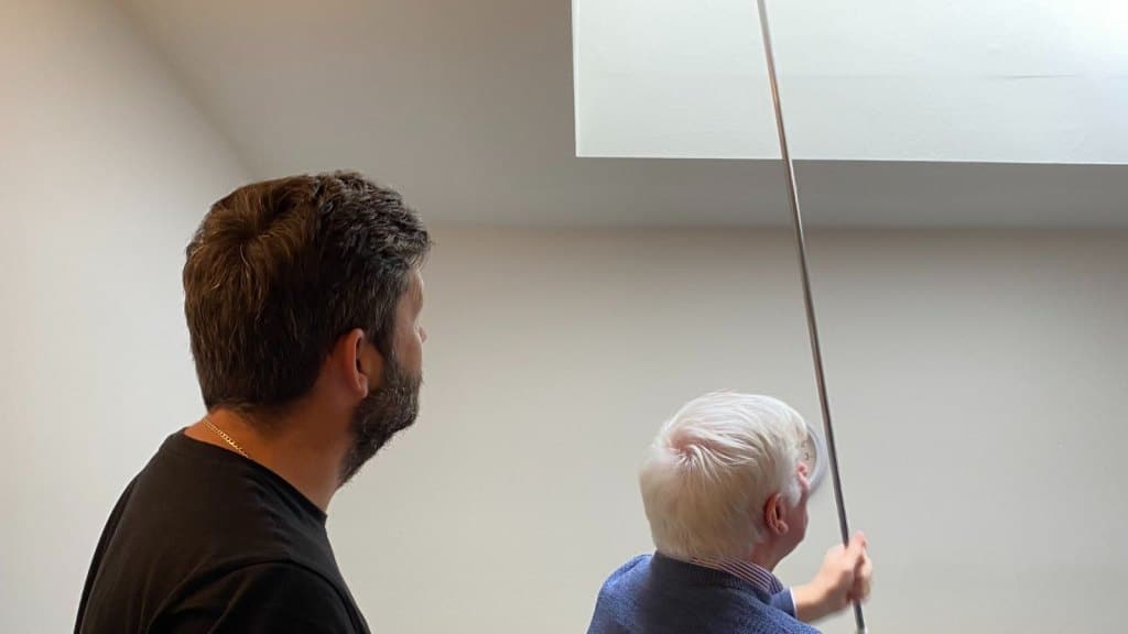 two men standing under a rooflight using a manual crank handle