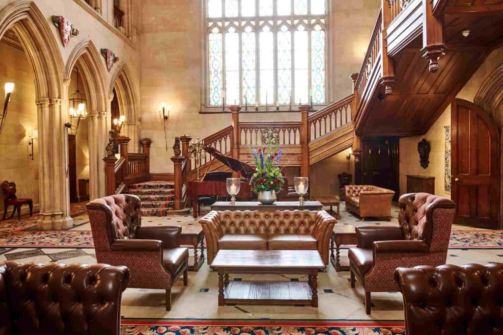 Hall room at hotel with sofas surrounding a coffee table, grand staircase to the right and grand piano in the background