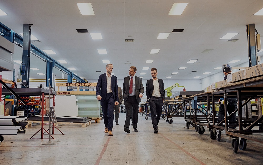 three men walking along the path in a rooflight factory wearing suits and looking at each other