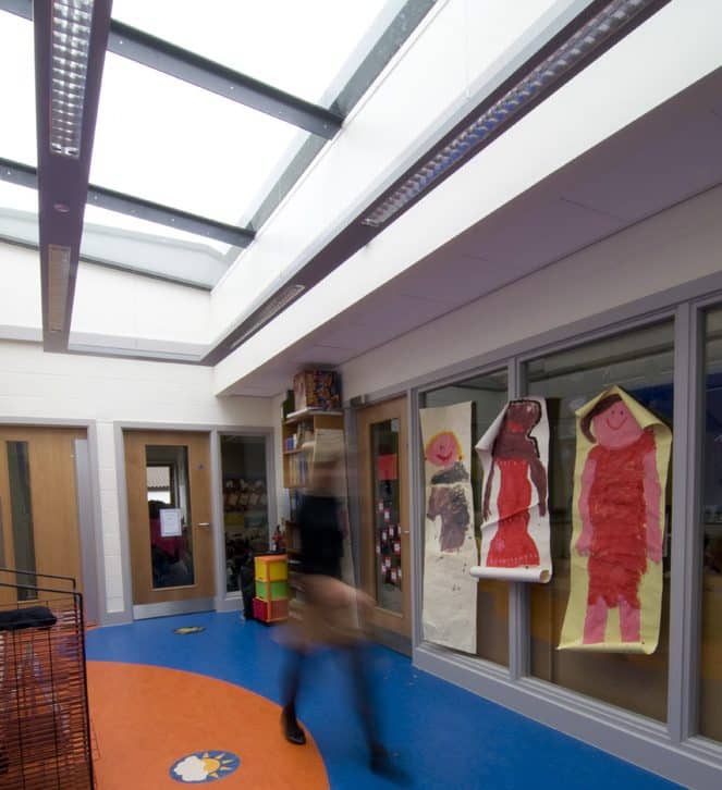 woman walking in school classroom, large multipart rooflight installed above